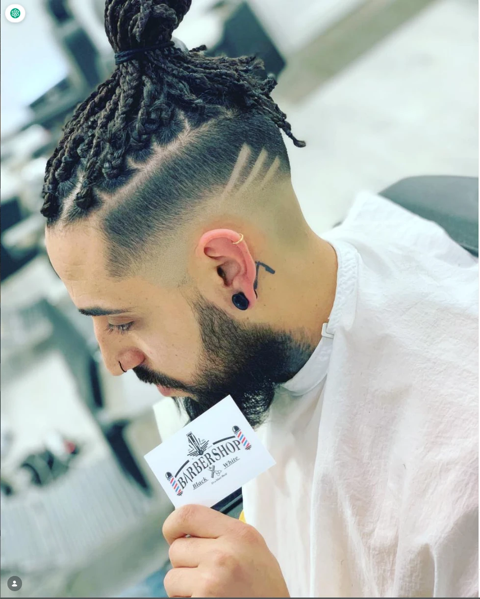 Corte con degradado y trenzas, hecho en Black&White Barbershop, con la tarjeta de la barbería en la mano